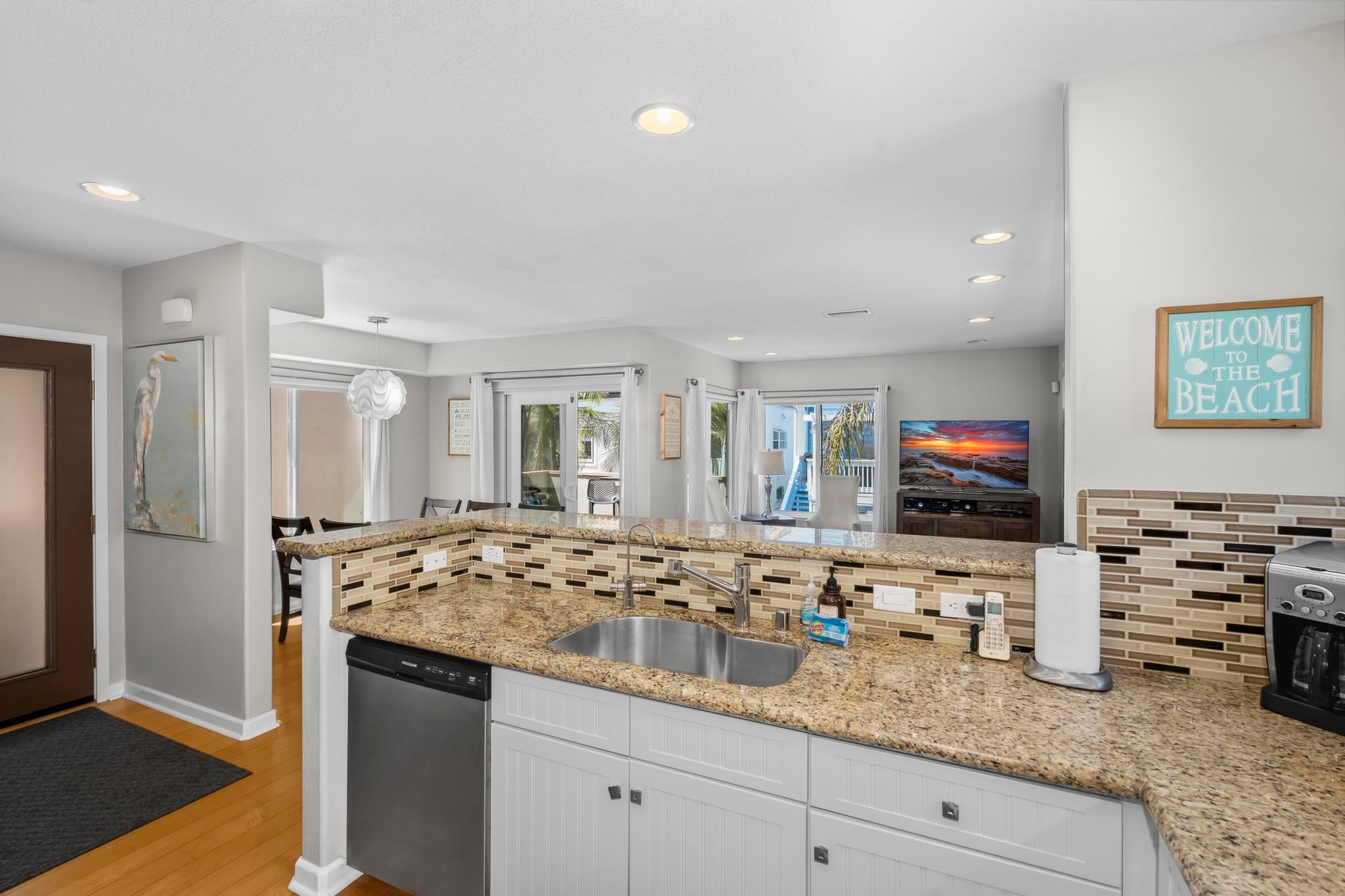 The kitchen at Belmont Beach House, open to the living room with a granite island and white cabinets