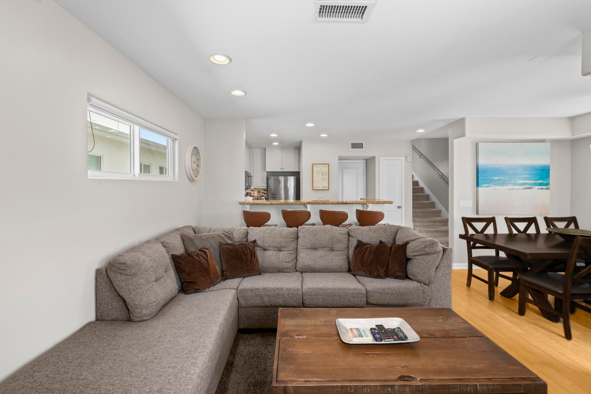 The living room at Belmont Beach House: a grey sectional, a wood coffee table, the dining table and the stairs beyond