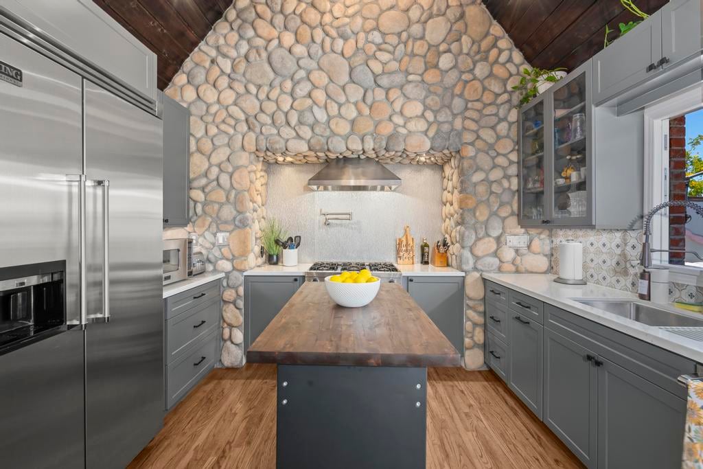 The kitchen at Kensington Canyon: a river-rock wall behind the range, grey cabinets and the rolling tool-chest island with its butcher-block top