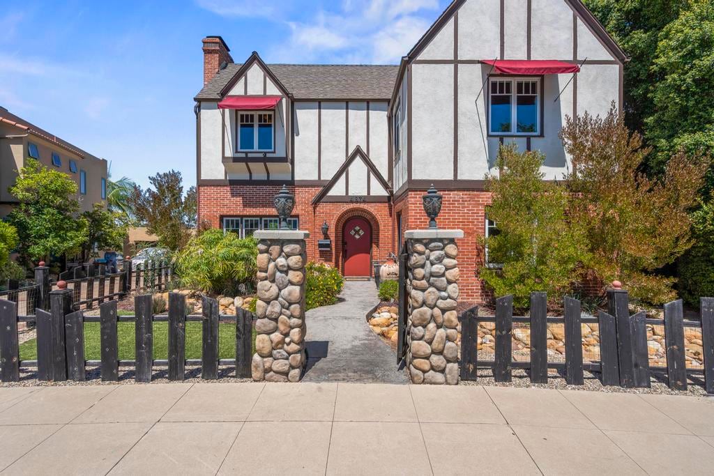 Kensington Canyon from the street: a brick and half-timbered Tudor with a red door, behind a river-rock wall and dark picket fence