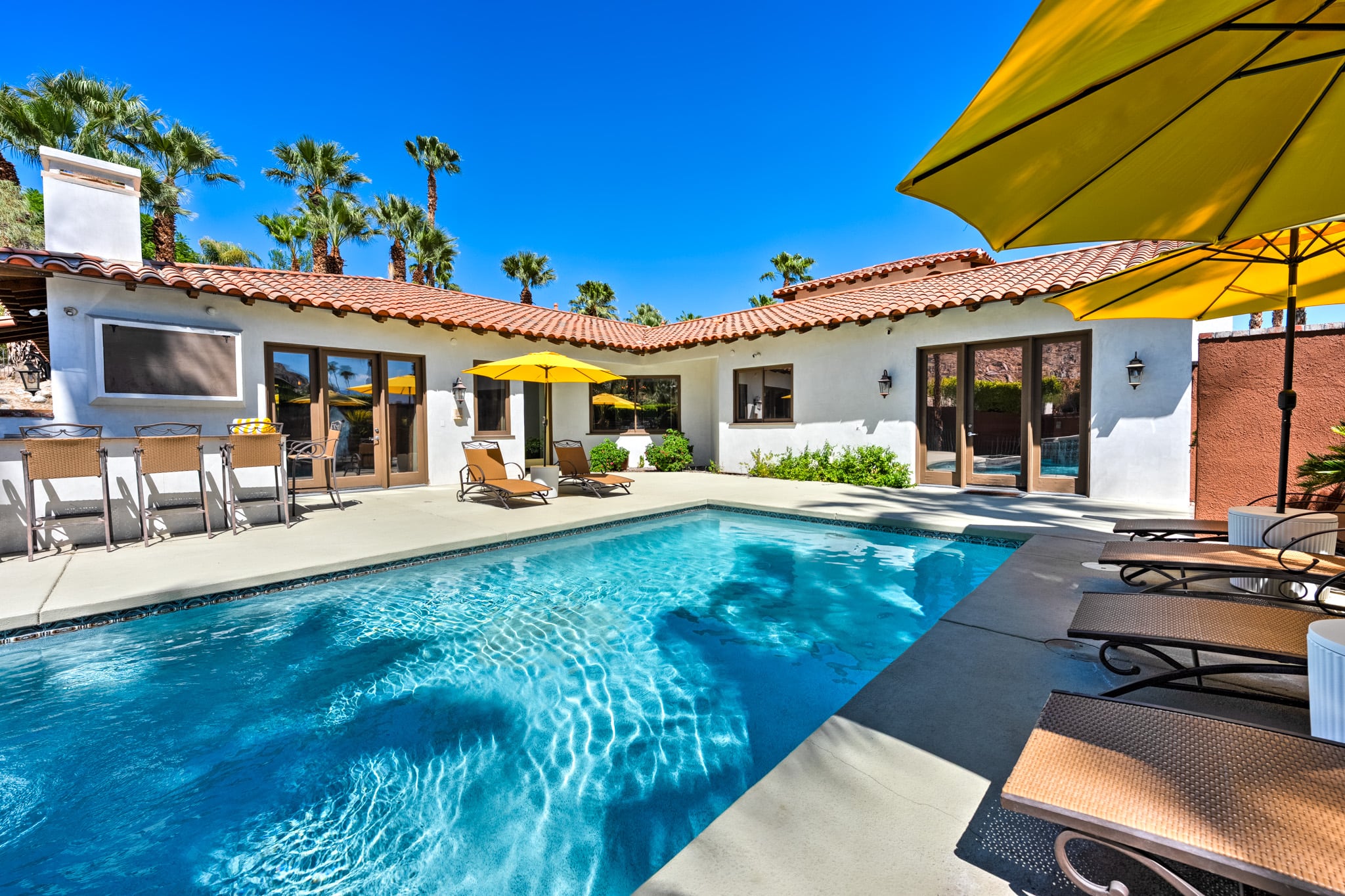 The pool at Mercury Palms in daylight with yellow umbrellas and the white villa behind
