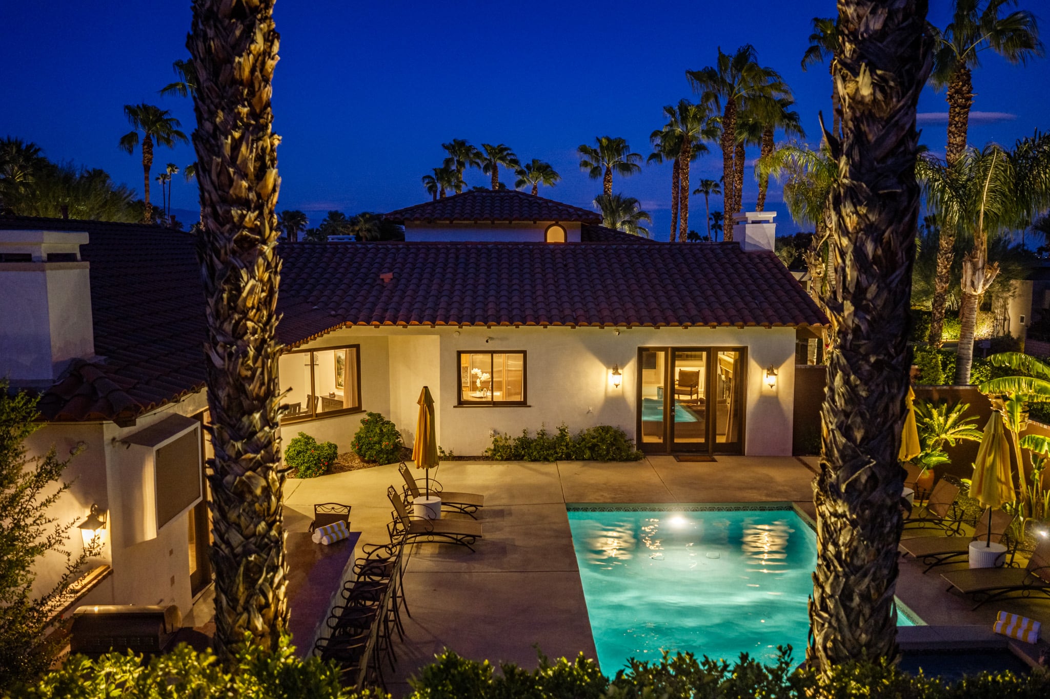 Mercury Palms at dusk from across the pool, the house lit and palms silhouetted against the sky