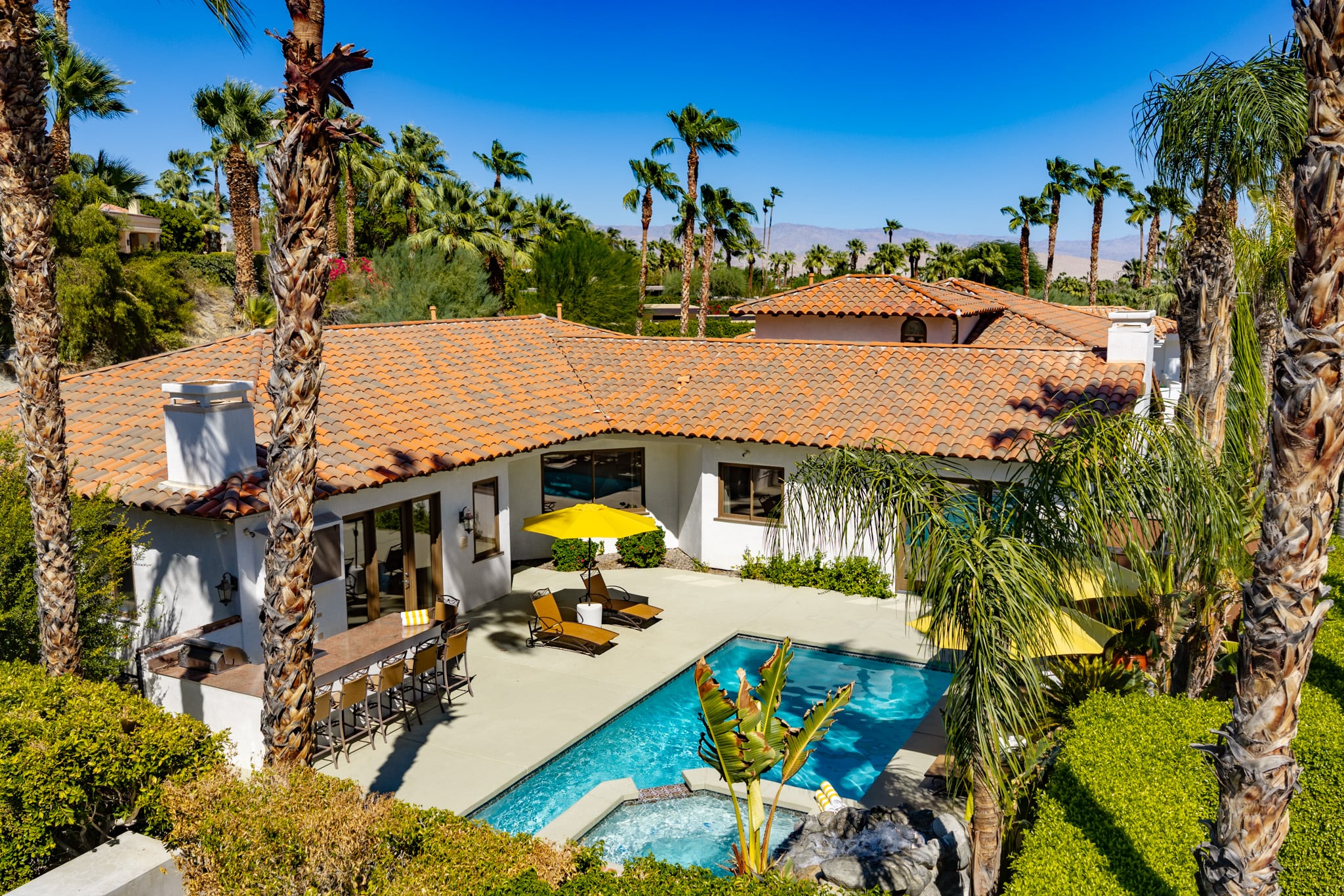 Mercury Palms from above: the tile-roofed villa, pool and spa set among tall palms with the mountains beyond