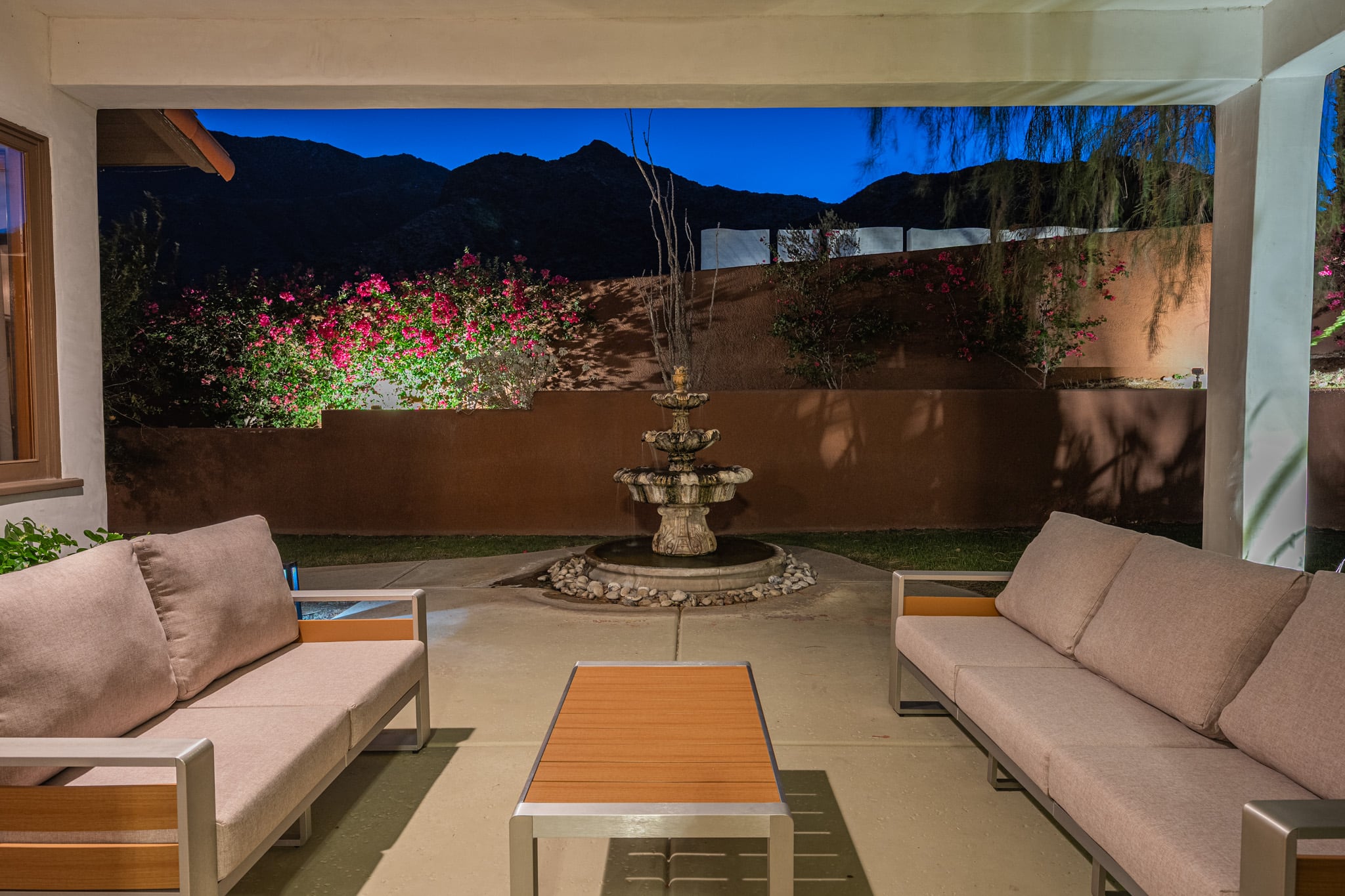 A covered patio at Mercury Palms at dusk, with a fountain, bougainvillea and the mountains behind the wall