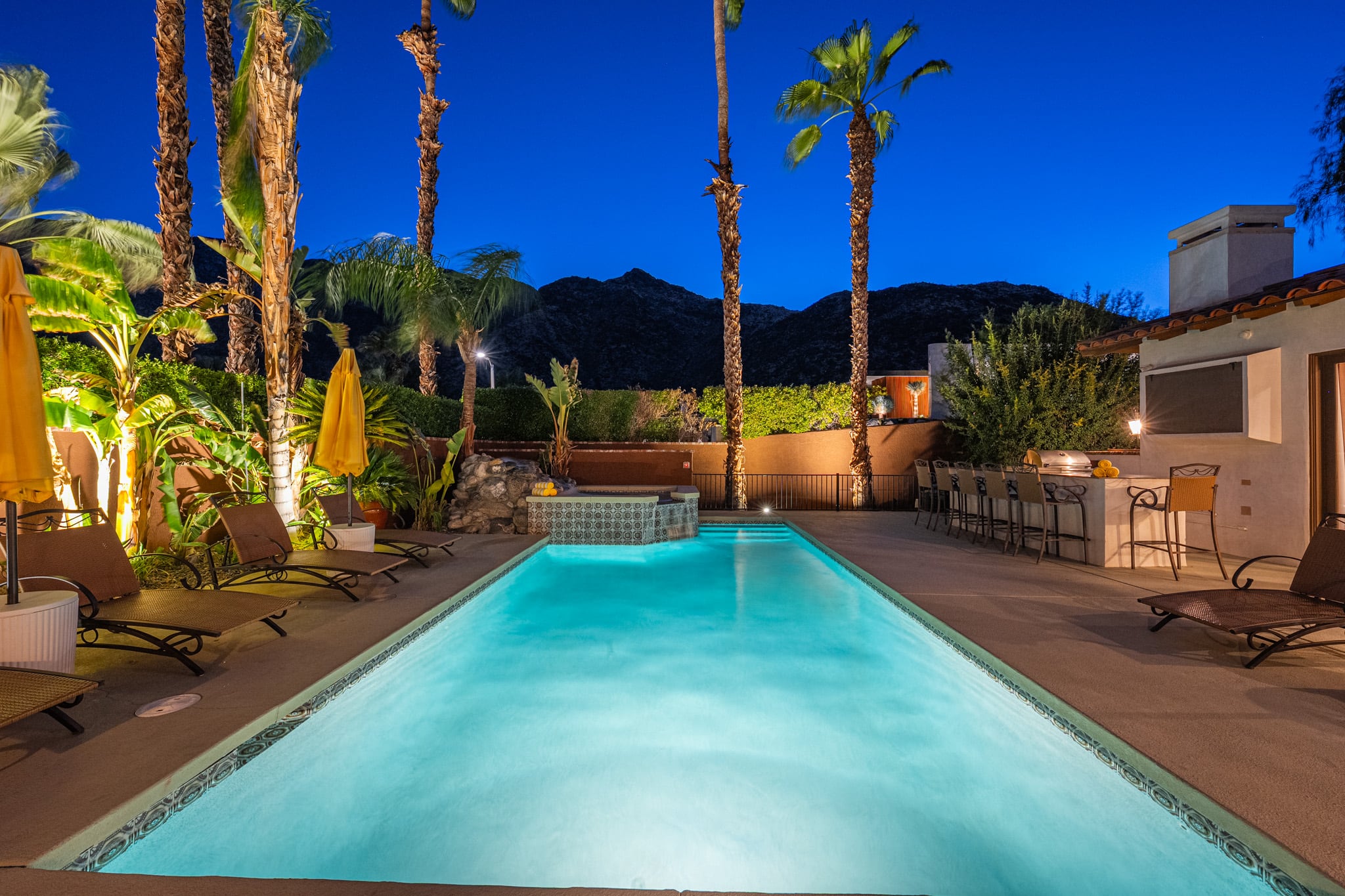 The Mercury Palms pool lit at dusk, ringed by palms with the mountains behind