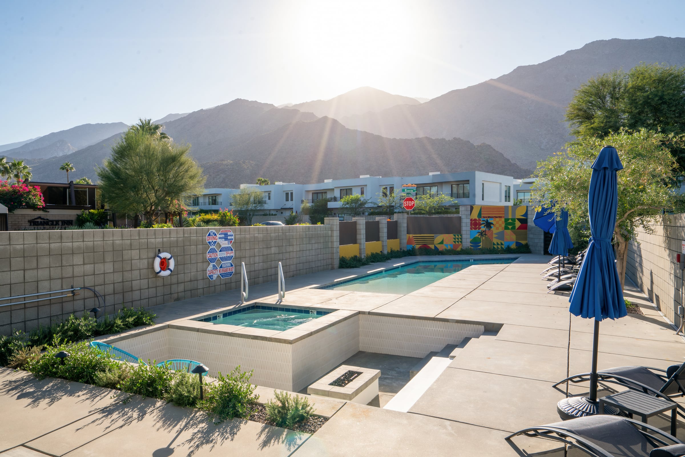 The Querencia Palms pool in afternoon sun with the mountains behind and a blue umbrella at the edge