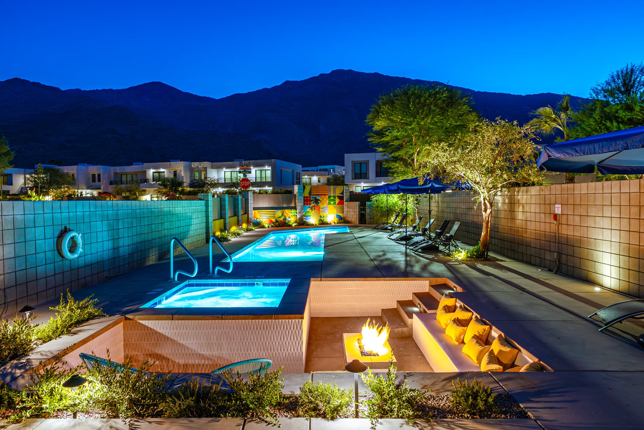 The Querencia Palms pool and spa at dusk, with a sunken fire-pit lounge, the residences lit behind and the San Jacinto Mountains above