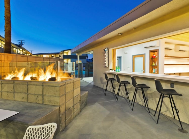 The outdoor fire pit and bar at The Cole at dusk, with black stools at the counter and the pool beyond