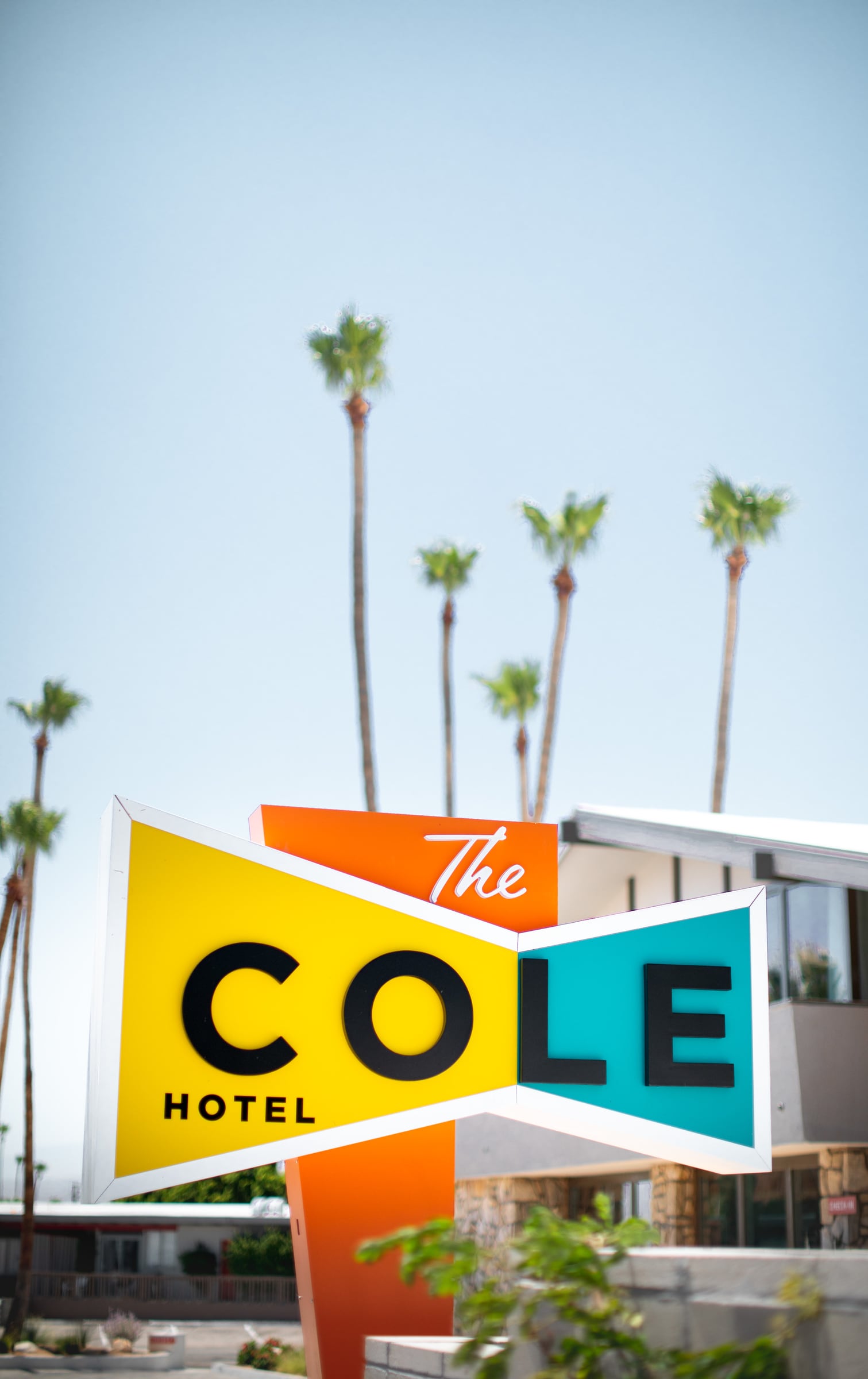 The Cole Hotel roadside sign in yellow, orange and turquoise, with tall palms behind it against a clear sky