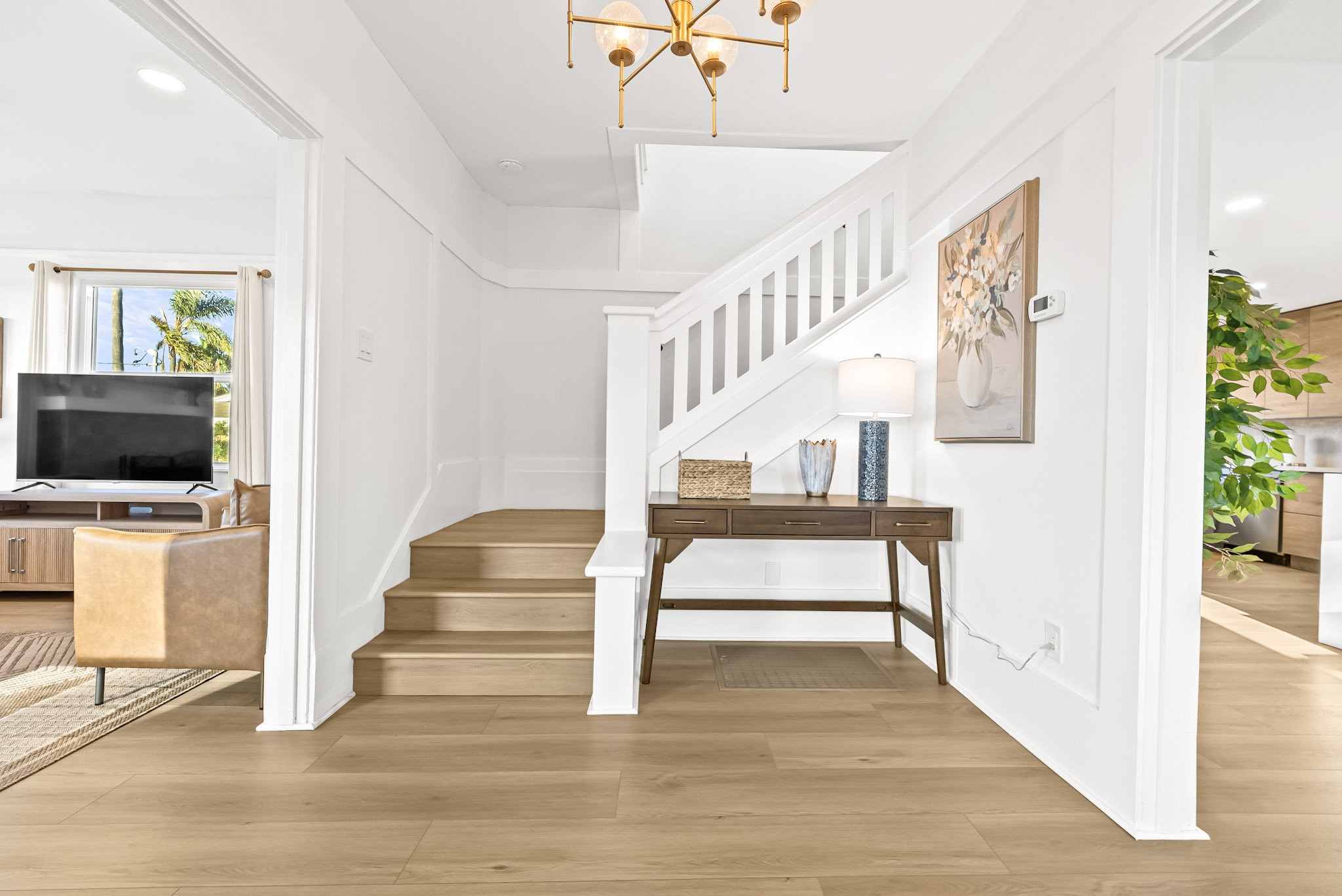 The entry at Vista Voltaire with the white staircase and square balusters, a walnut console table and a brass chandelier