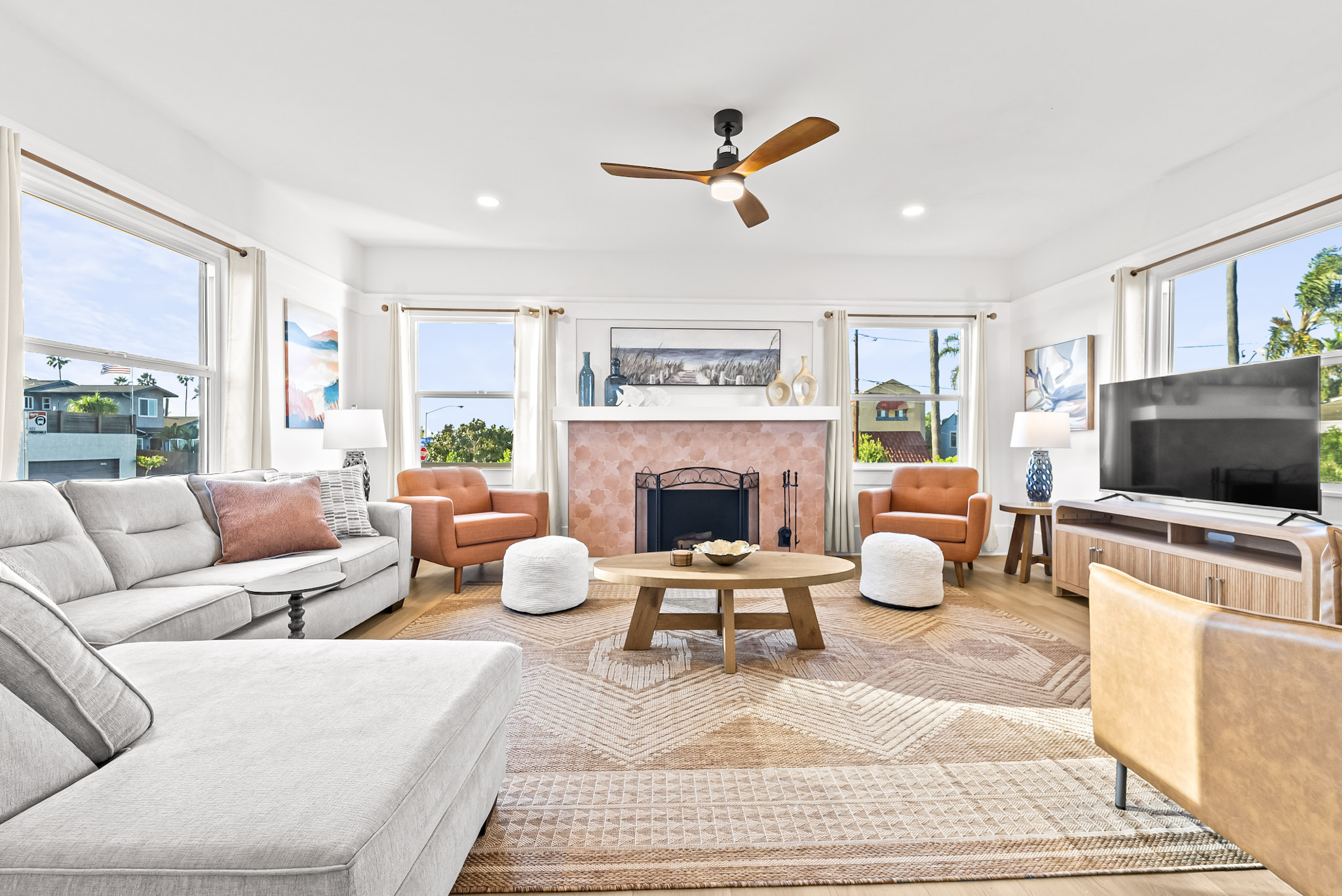 The living room at Vista Voltaire with a light sectional, two rust armchairs, a round oak coffee table and the original fireplace faced in terracotta tile